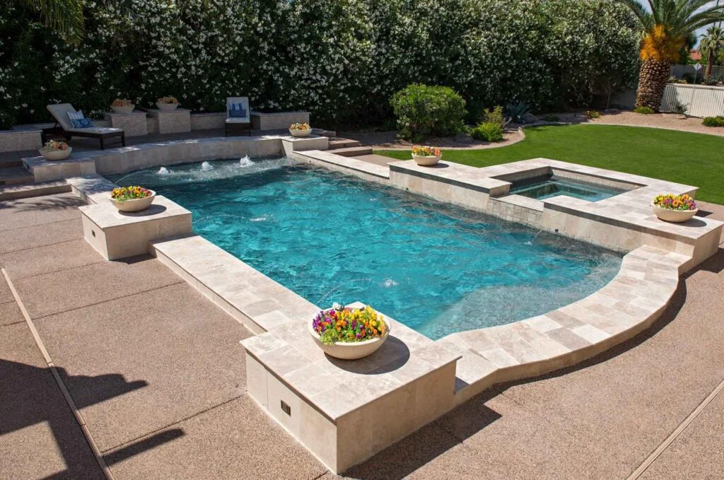 Backyard pool oasis with spa waterfall flowing over edge, tanning ledge and water feature