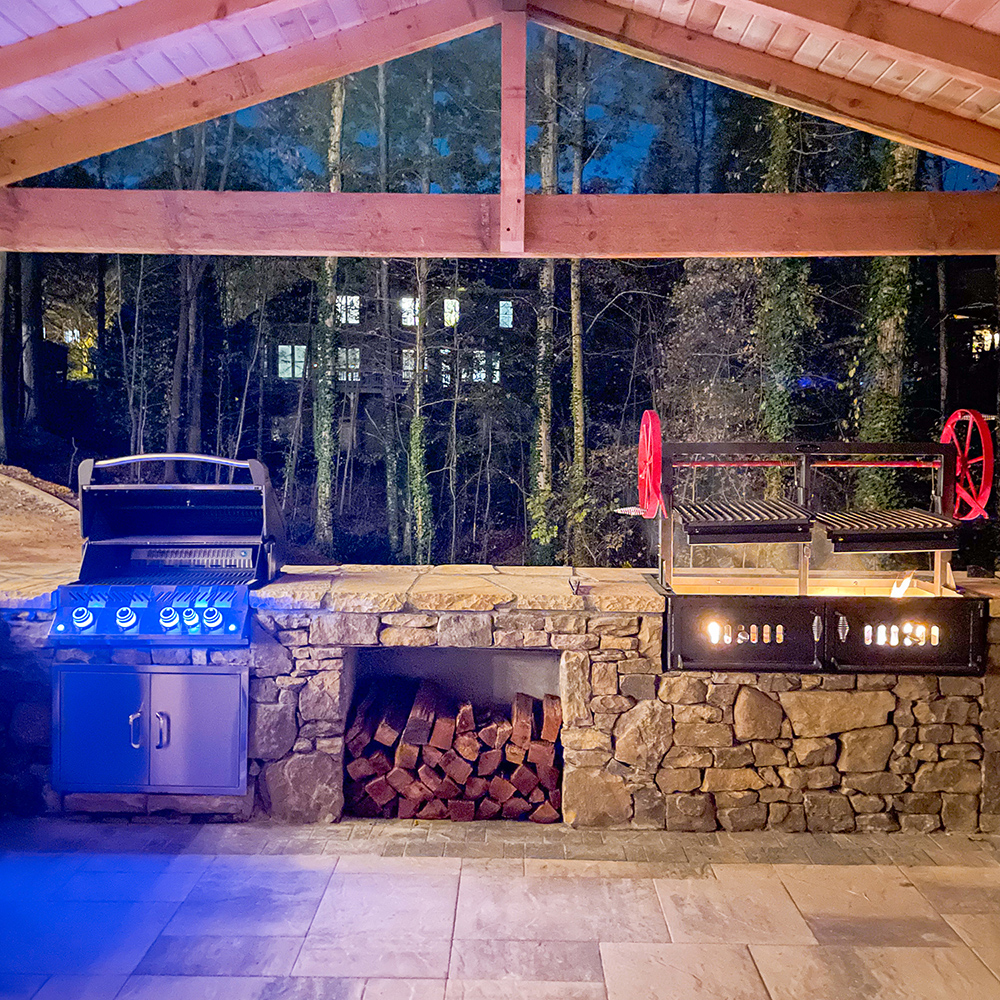 Outdoor kitchen with Santa Maria grill, storage for wood and electric grill inset in stone wall underneath cedar pavilion designed and installed for Kennesaw, Georgia homeowner.