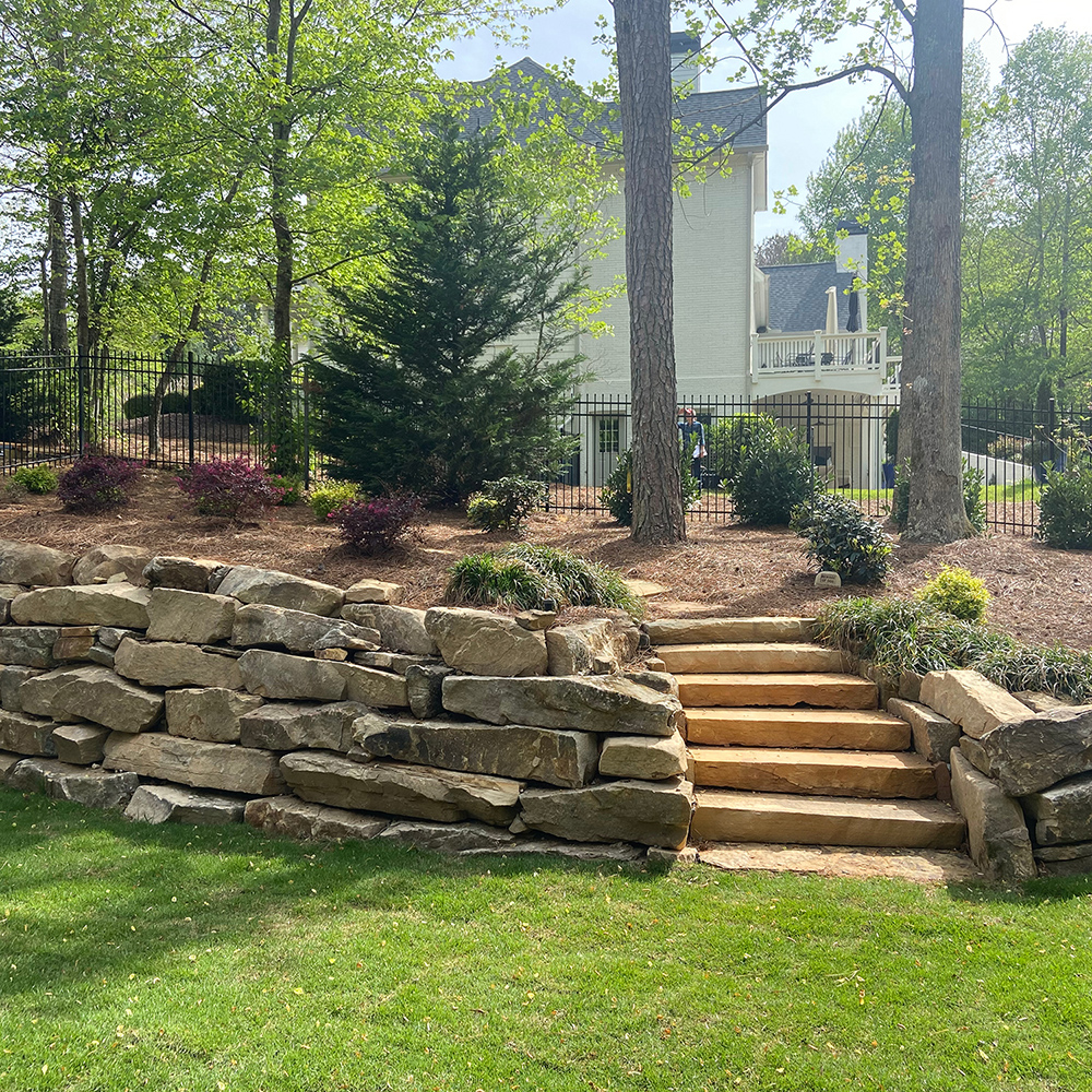 Boulder retaining wall with stone steps leading down into fresh sod landscape, designed and installed for Dallas, Georgia homeowner.