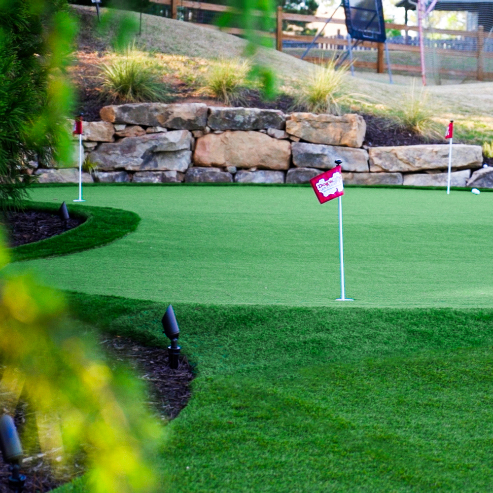 Artificial grass putting green with boulder wall designed and installed for Dallas, Georgia homeowner.